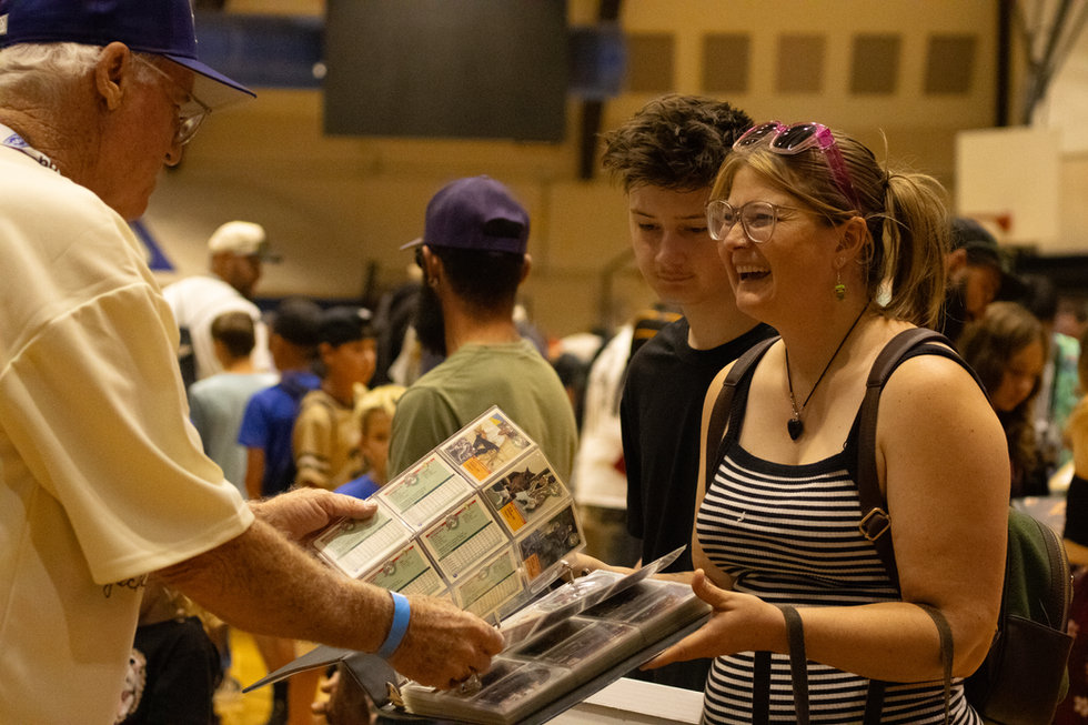 Collectors smiling as they look through a trading card binder at the PTCC show